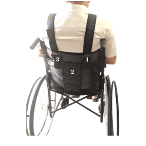 Foto ilustrativa das costas da cadeira de rodas para o cinto de segurança colete peitoral e pélvico, mostrando a numeração de encaixe, um e 3 as alças para o peitoral, e 2 para o pélvico, modelo de costas na cadeira com uma camiseta bege , pele clara e cabelos grisalhos.